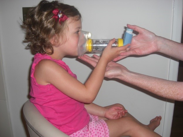A child being given an inhaler through a spacer
